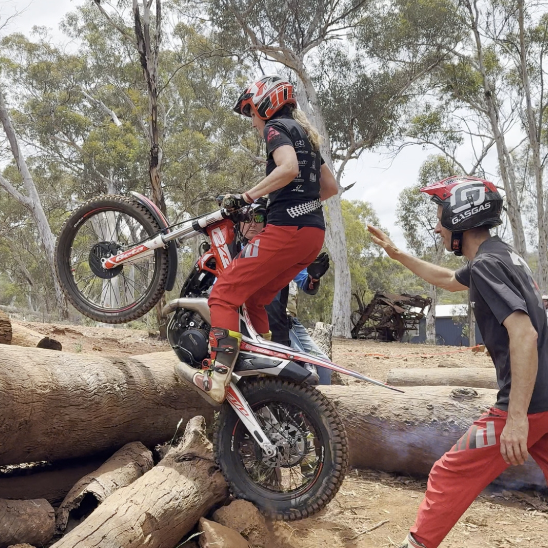 Trials rider lifting the front wheel over a log with instructor guidance